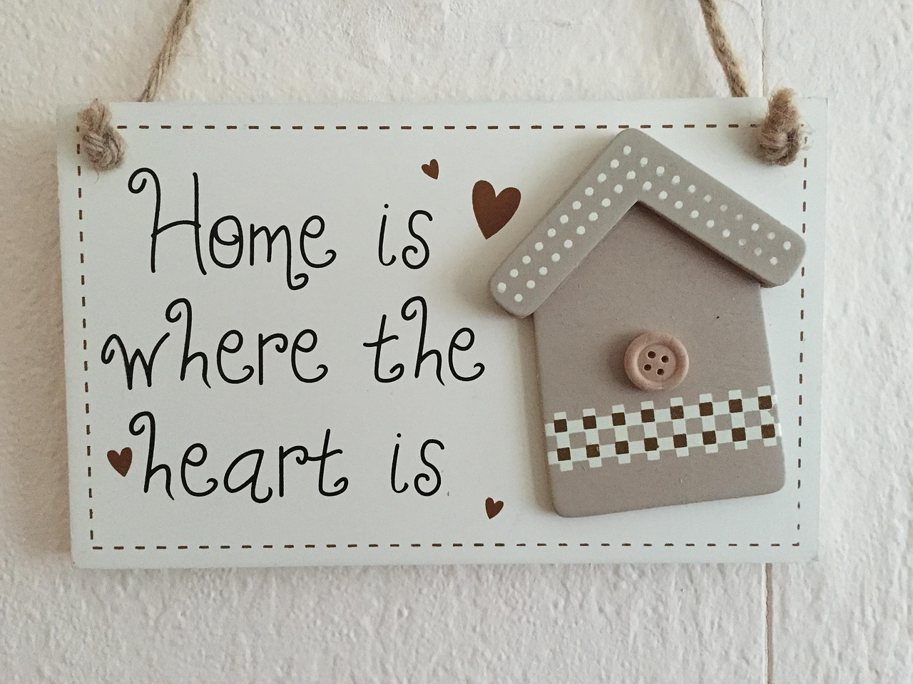 Wooden sign reads "Home is where the heart is," featuring a small decorative house and hearts, symbolizing love and comfort in the home.