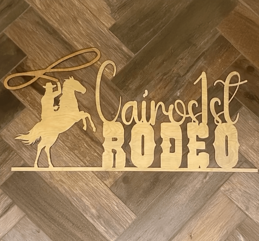 Cairo's 1st Rodeo wooden sign features a silhouetted cowboy on a horse, emphasizing the event's western theme. Ideal for promoting the rodeo.