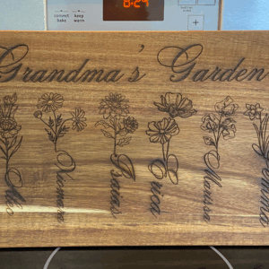 Wooden cutting board engraved with "Grandma's Garden," featuring illustrations of flowers and names: Denver, Elie, Vinas, Erica, Melissa, Gemma, and Antonio.