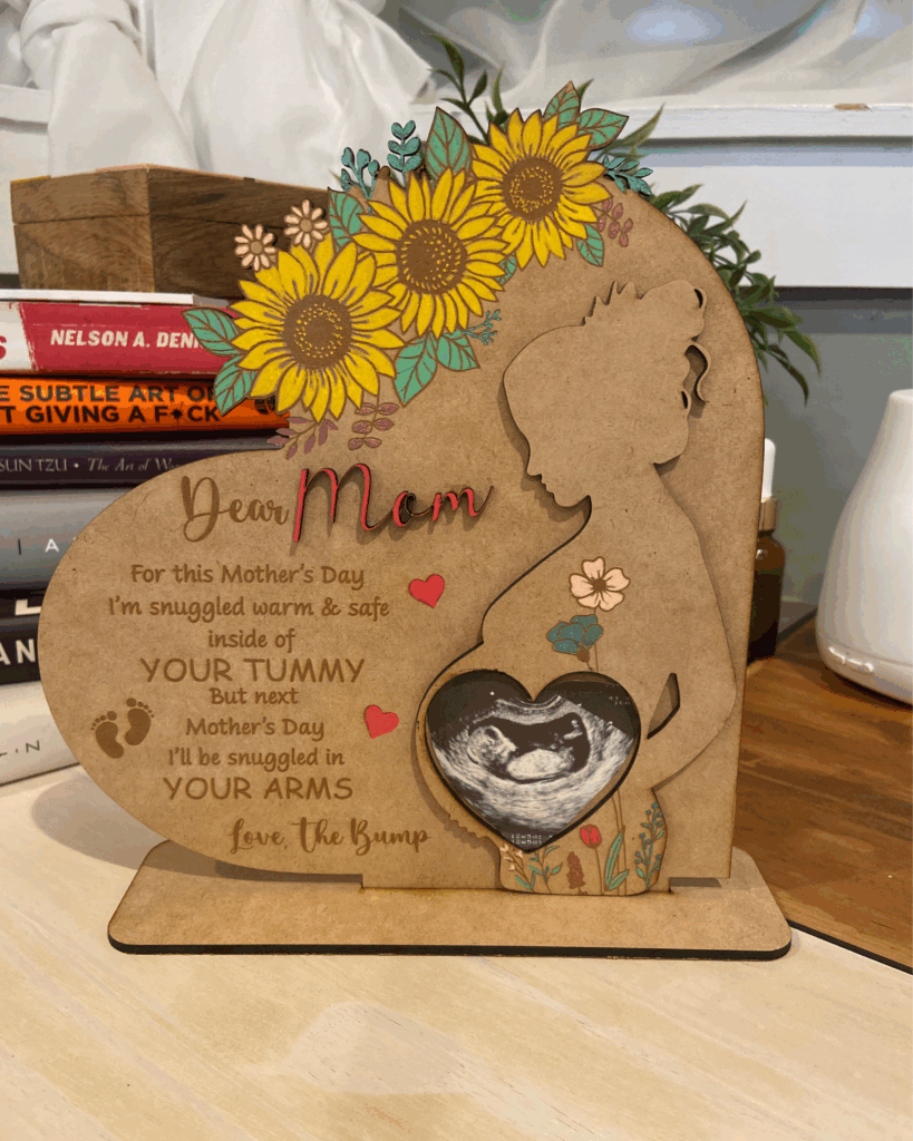 A heart-shaped plaque for Mother's Day, featuring a silhouette of a pregnant woman, flowers, and a sonogram image, celebrating maternal love and upcoming motherhood.