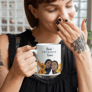 Woman in a black blouse smiles while holding a mug that reads "Best Coworker Ever," featuring illustrated faces and flowers.